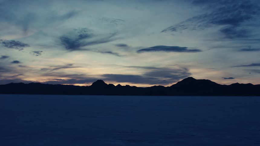A vast and serene landscape of a salt flat at twilight with silhouetted mountains against a moody sky