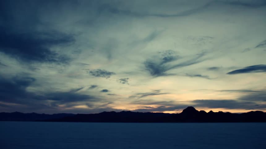 A slow pan reveals the vast expanse of a desert salt flat under a dramatic, cloudy sky at twilight