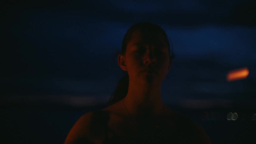 A contemplative young woman at dusk is illuminated by the light from two sparklers she holds