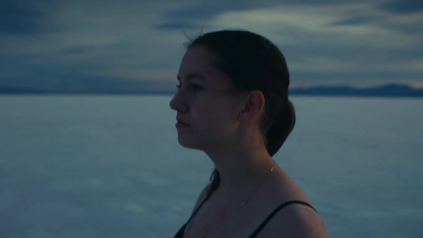 A contemplative young woman looks into the camera before turning and walking away across the vast, empty salt flats at sunset