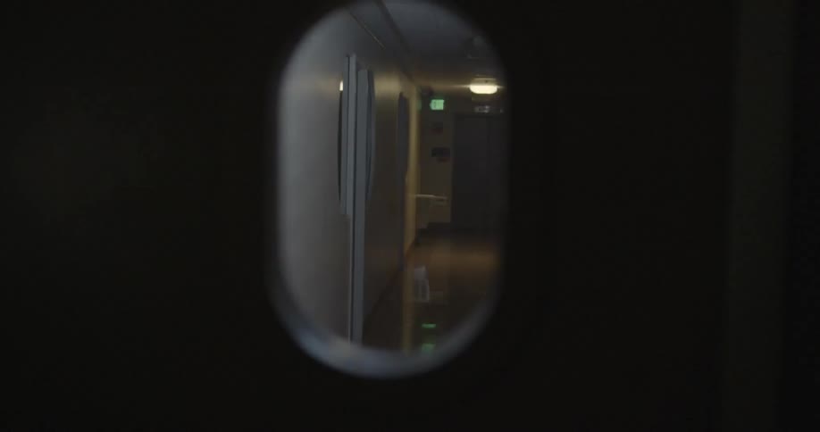 View looking through a keyhole at a woman walking down a hallway