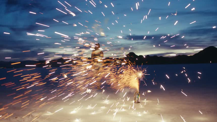 A woman stands still as a fountain firework explodes in front of her on the Bonneville Salt Flats at twilight