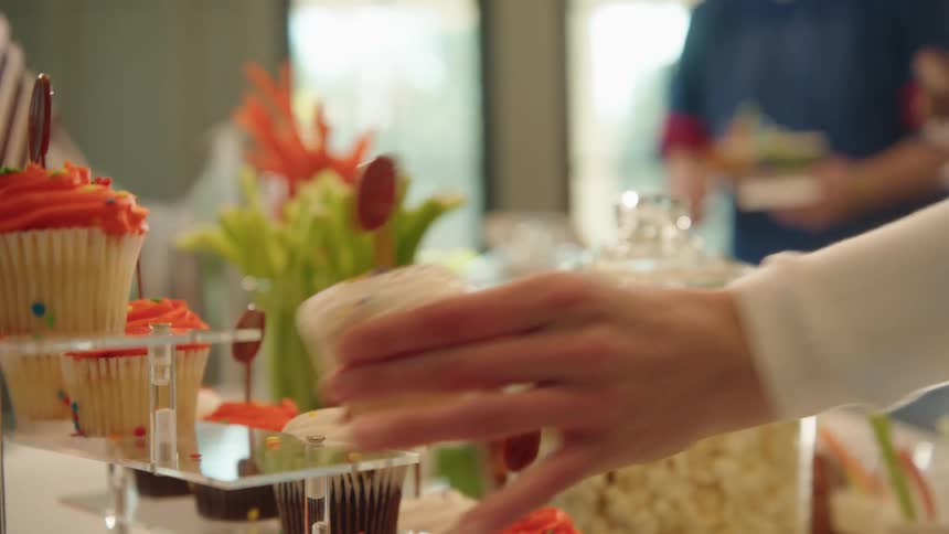 A hand reaches out in slow motion to grab a football-themed cupcake from a party snack table