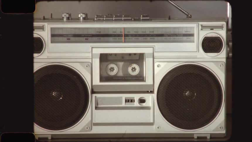 A vintage silver boombox plays a cassette tape, captured with a nostalgic old film aesthetic including grain and scratches