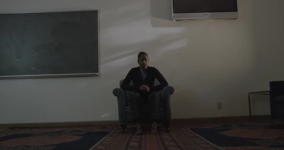 Woman sitting on chair in room looks down with eyes closed