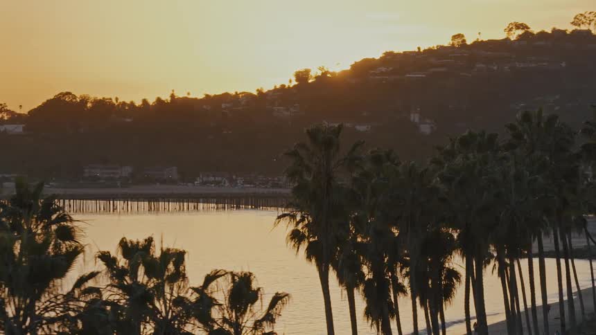 A picturesque view of the Santa Barbara coastline with palm trees silhouetted against the golden sunset over the ocean