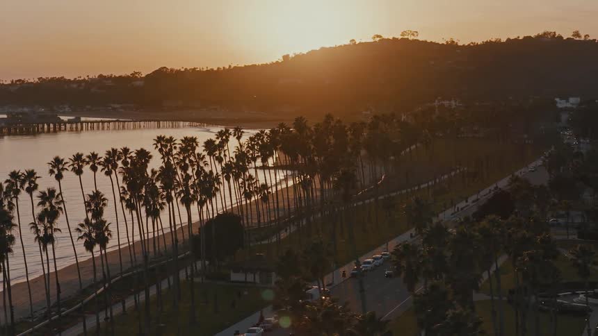 A stunning aerial shot reveals the palm-lined Santa Barbara coast as the sun sets over the ocean and hills