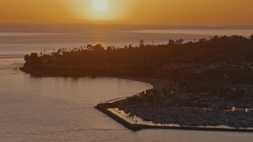 A serene wide shot of a coastal bay and marina basking in the golden light of the setting sun over the ocean