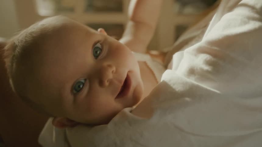 A beautiful newborn baby with bright eyes smiles contentedly while being held by their mother in a warmly lit room