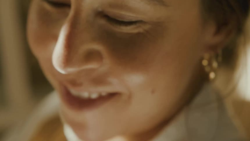 A serene woman smiles with her eyes closed, bathed in the warm, gentle light of a cozy room