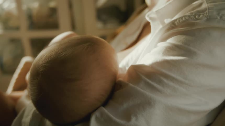 A mother tenderly breastfeeds her newborn baby in a soft, sunlit room, capturing an intimate moment of bonding and care