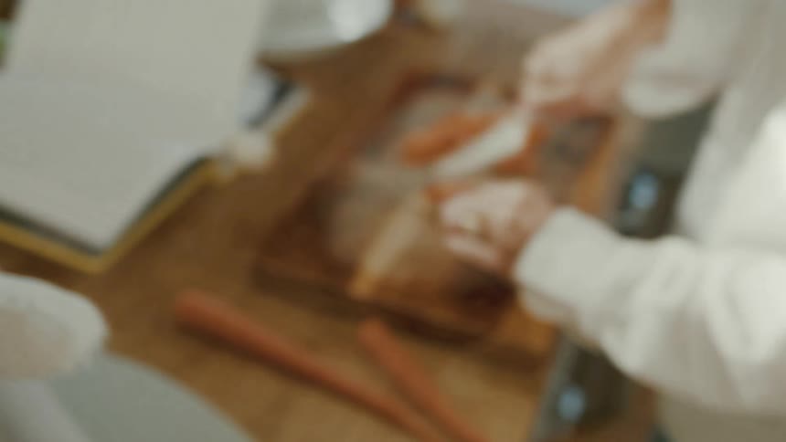 A close-up shot of a baby holding a stuffed bunny transitions to a person dicing carrots in a sunlit kitchen