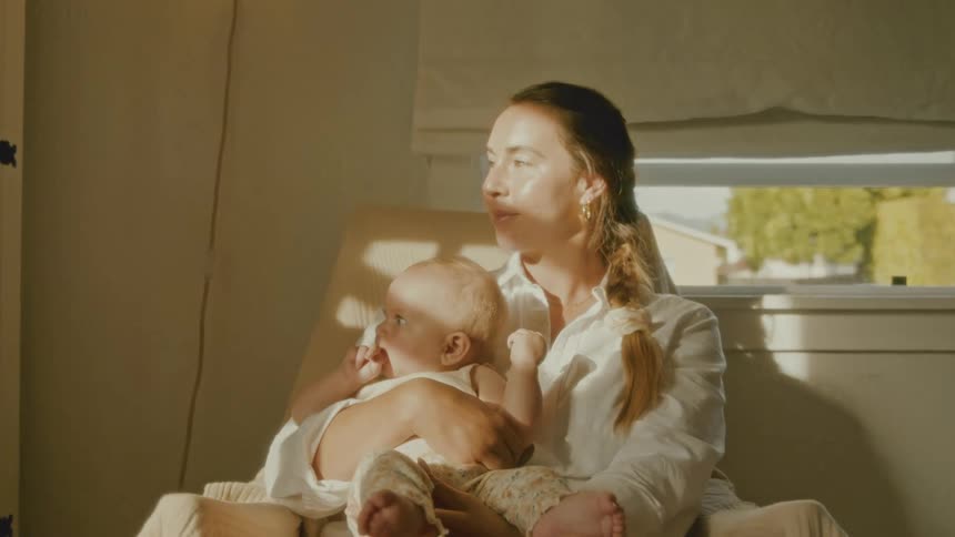 A serene mother holds her baby in a rocking chair, enjoying a peaceful moment in the warm sunlight streaming through the window