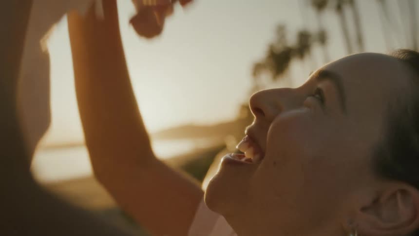A joyful mother lovingly lifts her newborn baby into the air, smiling and sharing a tender moment at sunset