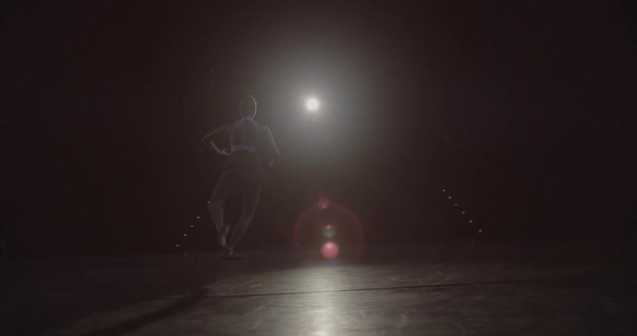 A dancer twirls and jumps on a dark stage