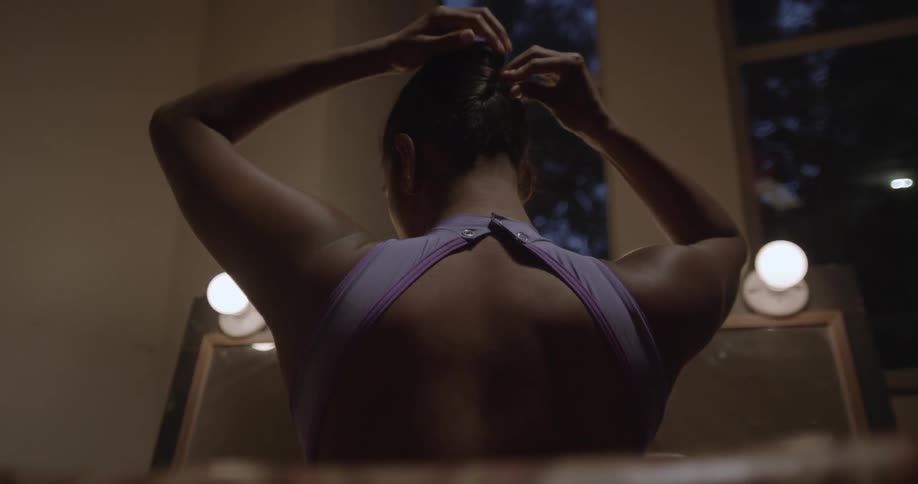 Woman standing in front of a mirror ties hair up