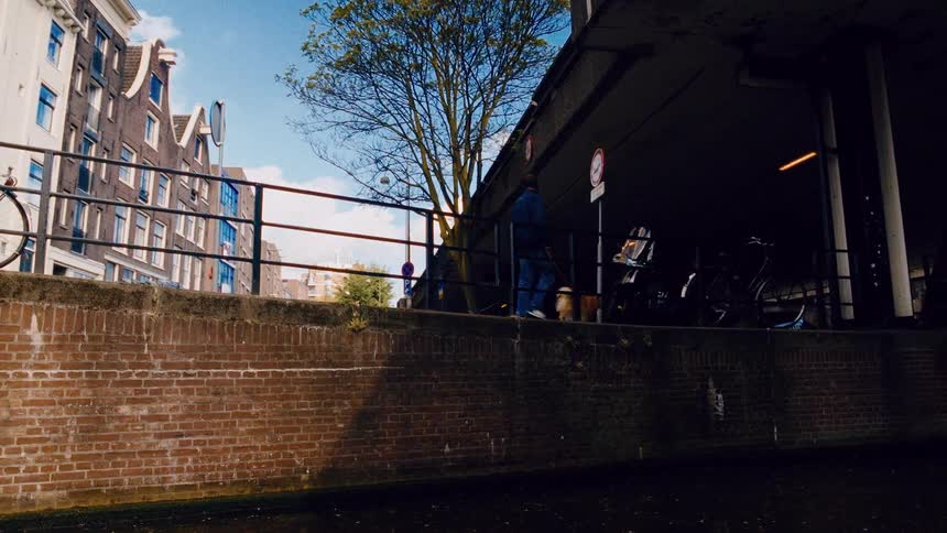 A man and his fluffy dog take a leisurely walk along a sun-drenched canal path in Amsterdam