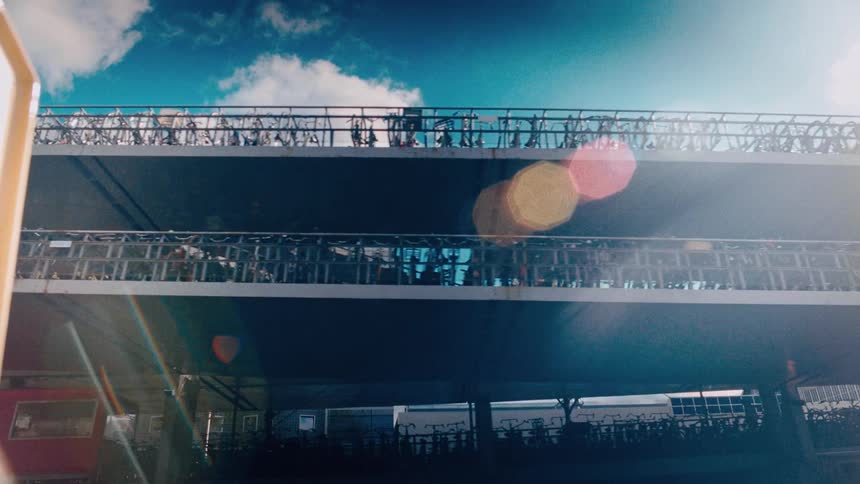 A sun-drenched, low-angle view of a multi-story bicycle parking garage with a train passing by on a bright day