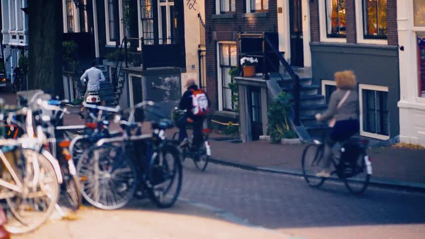 A slow-motion shot of people riding bicycles down a charming cobblestone street in Amsterdam