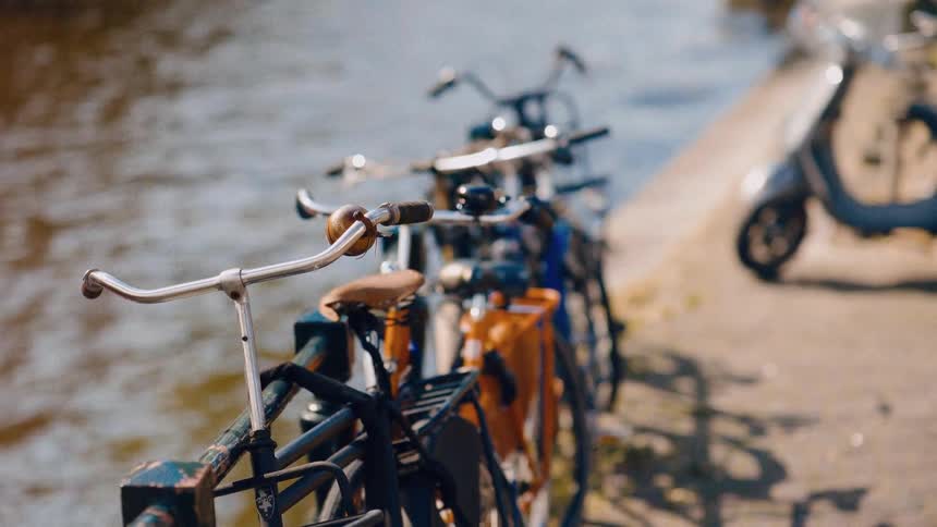 A row of vintage bicycles are parked next to a city canal on a bright, sunny day