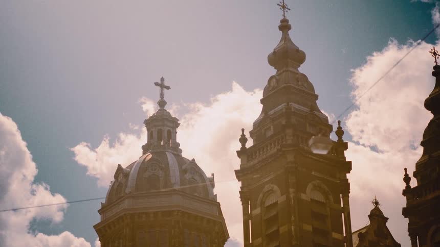 Majestic sunlit towers of an old European church stand tall against a cloudy blue sky