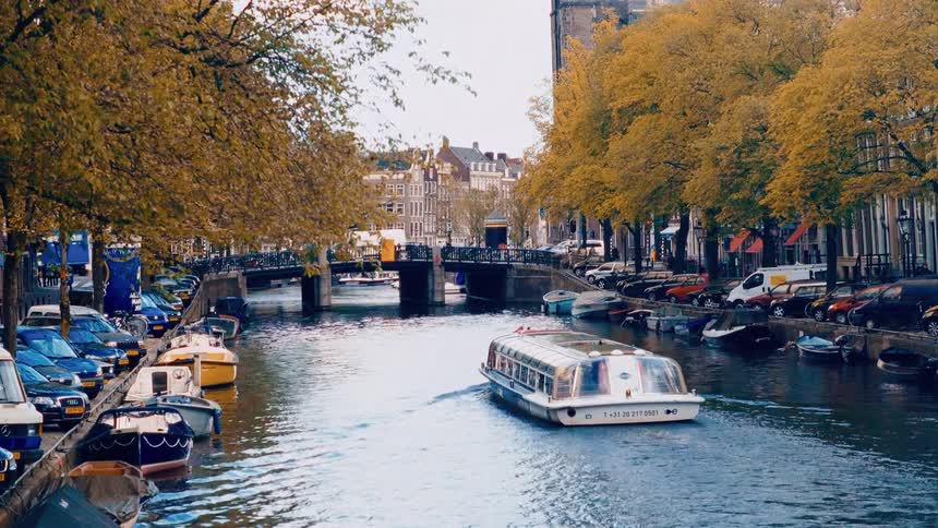 A tour boat cruises down a scenic canal in Amsterdam during a beautiful autumn day