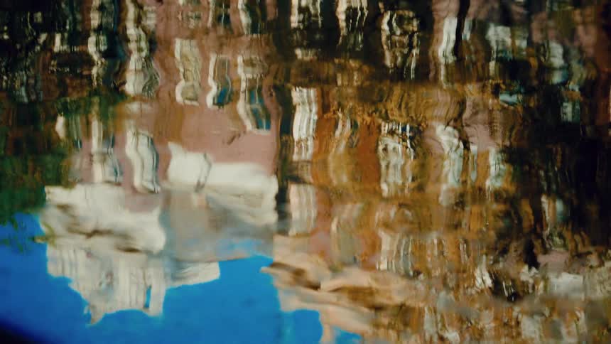 Colorful city buildings create an abstract, impressionistic painting on the rippling water's surface