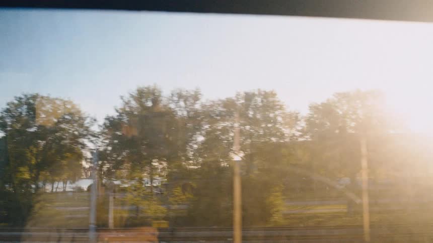 A scenic view of a sun-drenched park and cityscape from the window of a moving train