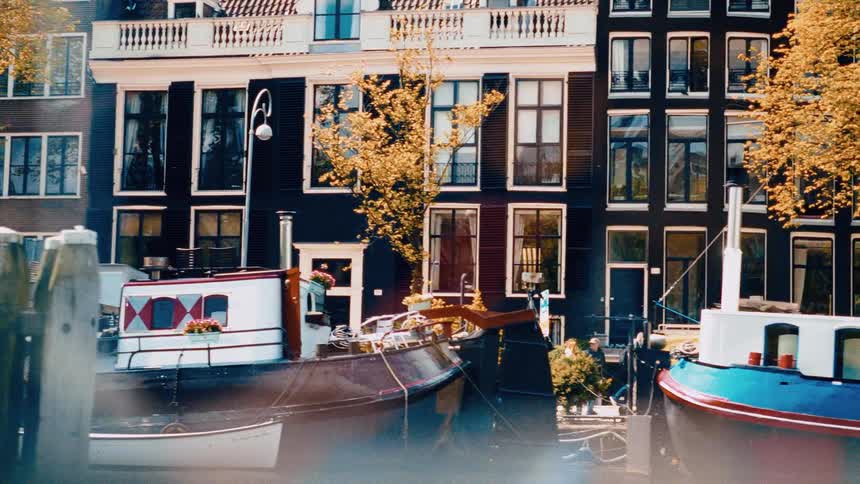 Dreamy panning shot of houseboats and traditional Dutch architecture along a canal in Amsterdam during autumn