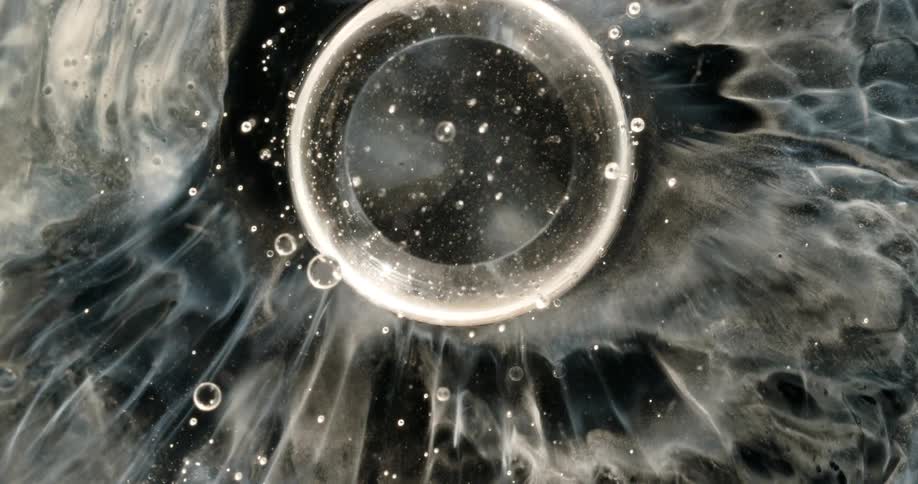 A cosmic-like bubble bursts in slow motion, creating a mesmerizing ripple effect in a swirling black and white liquid