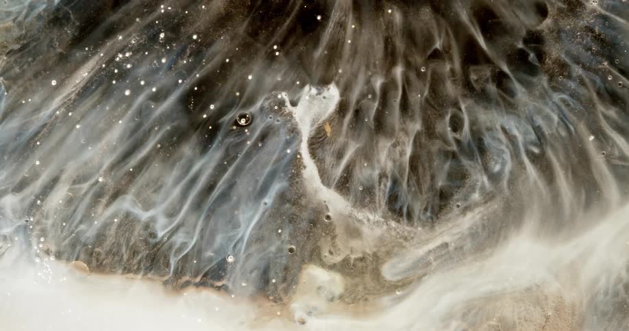 Ethereal white and brown liquids swirl in a dark, glittery mixture, creating a cosmic, abstract background