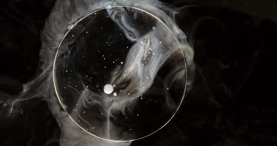 Ethereal white smoke swirls around a glass sphere containing a miniature galaxy with stars and planets against a dark background