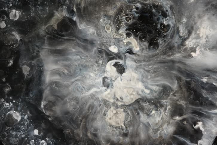 An abstract top-down view of black and white liquids swirling together to create a cosmic, galaxy-like pattern
