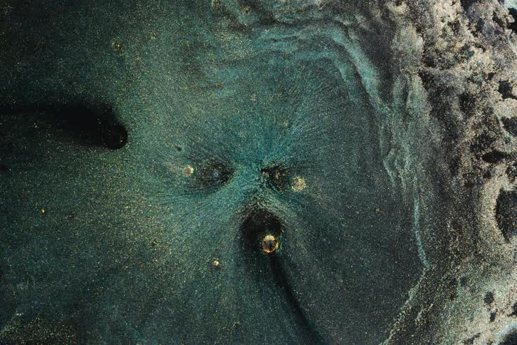 An abstract, cosmic vortex of dark teal and black liquid shimmers with gold glitter, slowly swirling outwards