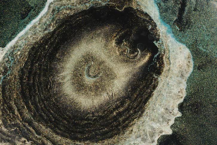 A mesmerizing top-down view of a swirling vortex of gold, silver, and black metallic particles in fluid art