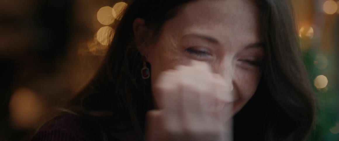 A close-up slow-motion shot of a beautiful mature woman laughing and smiling shyly with warm bokeh lights in the background