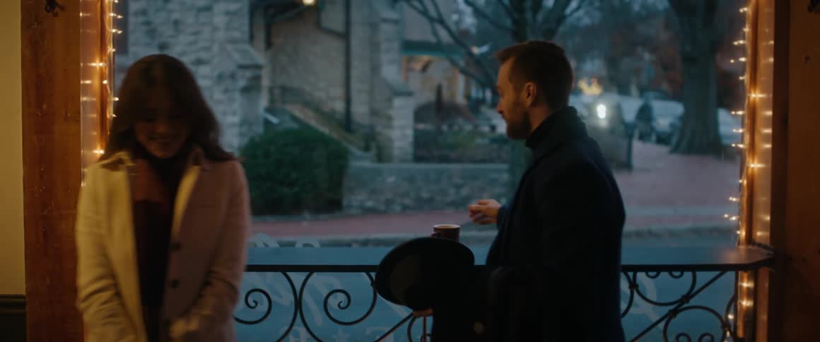 A well-dressed couple enjoys a pleasant conversation on a porch decorated with festive Christmas lights
