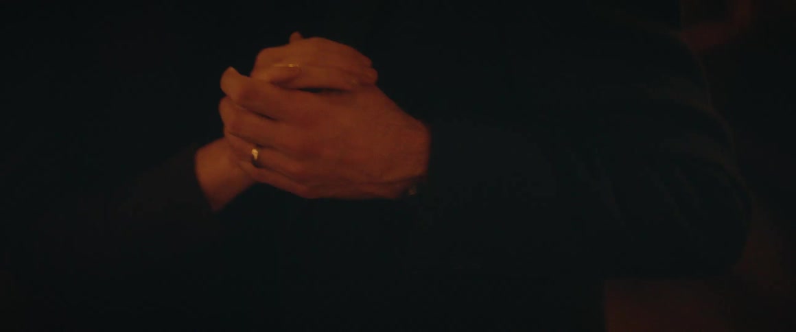 A romantic close-up of a couple's intertwined hands as they embrace and slow dance in a dimly lit setting
