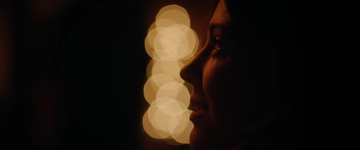 Close-up profile of a woman's silhouette smiling against a backdrop of warm bokeh lights at night