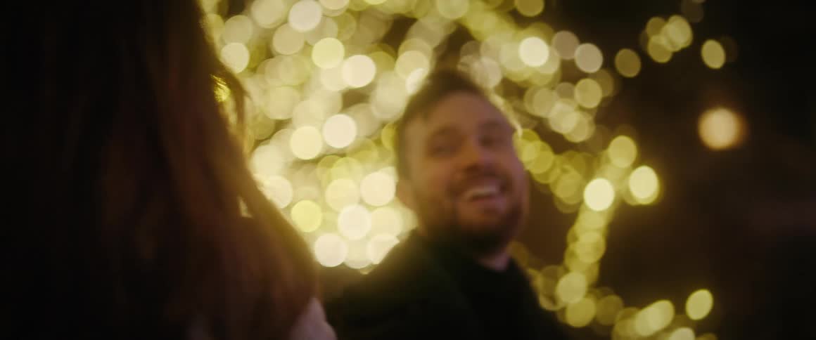 A happy couple laughs together on a romantic date at night, surrounded by festive bokeh lights
