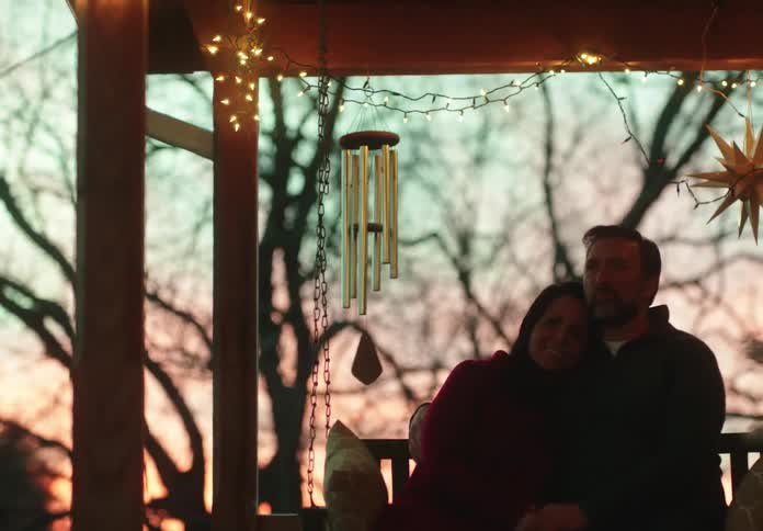 A happy couple cuddles together on a porch swing, enjoying the sunset and the warm glow of string lights