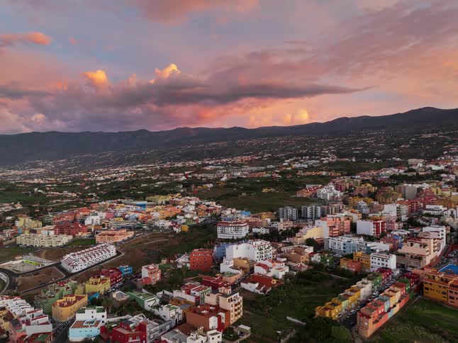 Stunning aerial footage shows a vibrant town nestled in a mountain valley as the sun sets, casting a warm glow on the colorful clouds