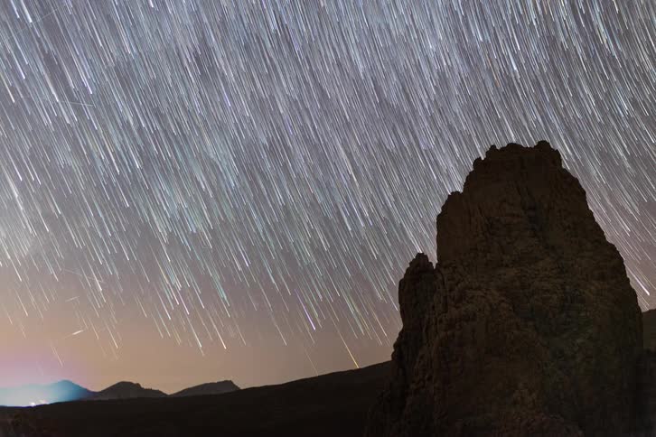 A breathtaking astrophotography time-lapse captures star trails streaking across the night sky above a dramatic rock formation