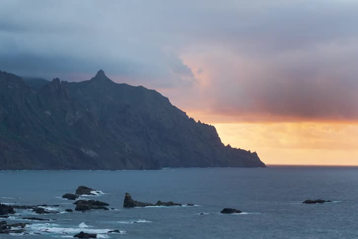 Dramatic timelapse shows moody clouds rolling over a rugged mountain coastline as the sun sets over the ocean