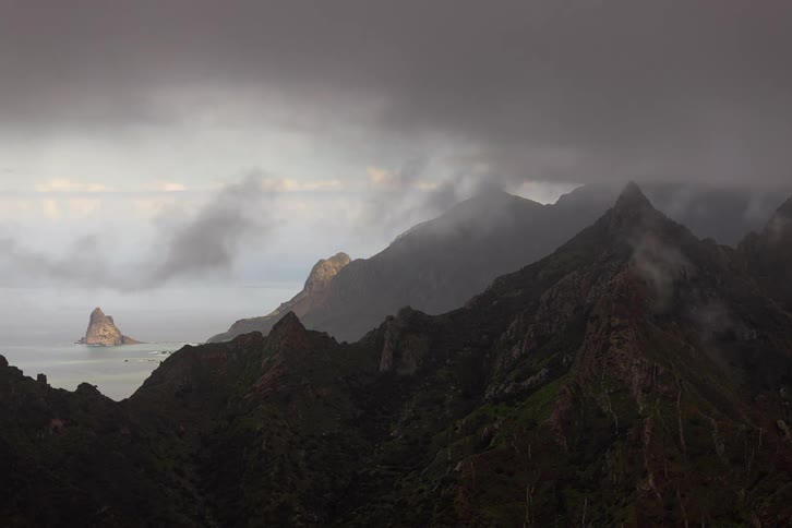 A dramatic timelapse of moody clouds and fog swirling over a rugged mountain range along the coastline