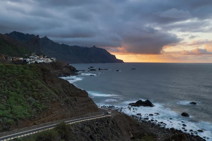 A stunning timelapse of a winding coastal road next to a small village and the ocean during a dramatic golden sunset