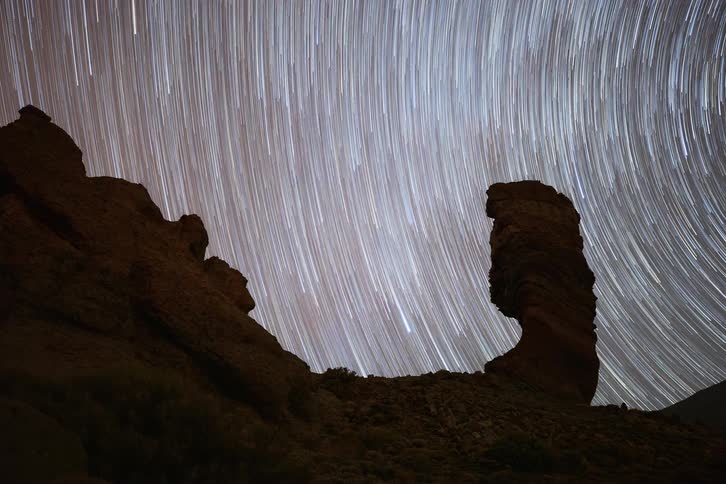 A stunning timelapse captures the rotation of the Earth as stars form trails across the night sky above a silhouetted rock formation