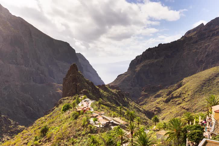 A scenic time-lapse of a lush green mountain village in a canyon with the ocean visible in the distance as clouds and shadows move across the landscape