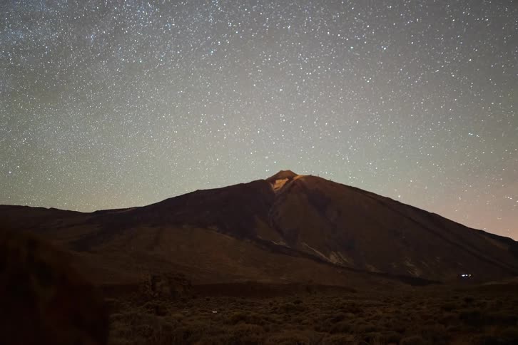 A stunning night timelapse reveals the Milky Way moving across the starry sky above a majestic mountain volcano, with the camera panning and racking focus