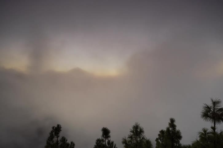 Mysterious fog and clouds sweep across a forested mountain landscape, revealing distant peaks at sunset in a beautiful timelapse